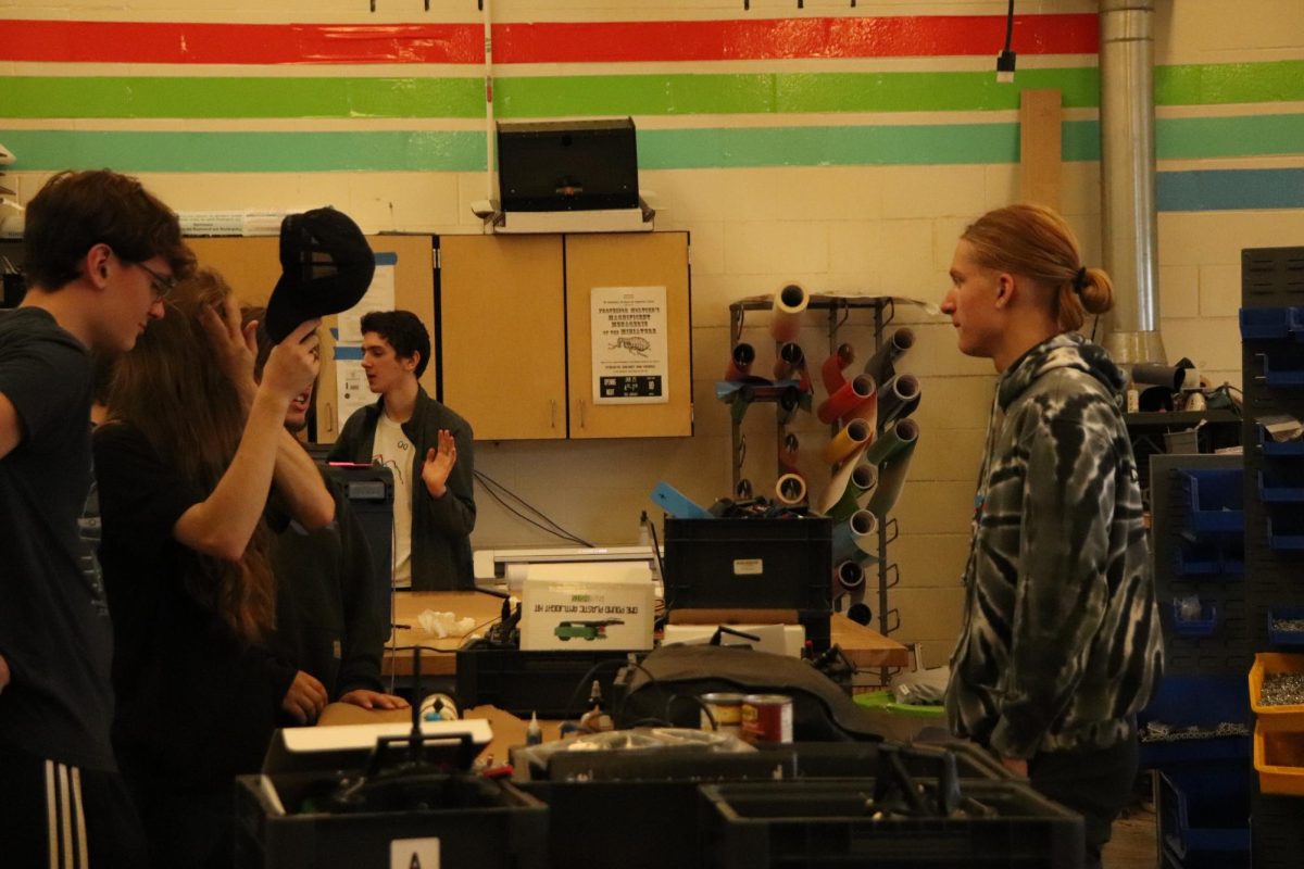 Designers Kasey Gridley (left with glasses) and Liam Frost (right) in the workshop. The two discuss allocating resources and machines between both of their teams, in order to have maximum efficiency.